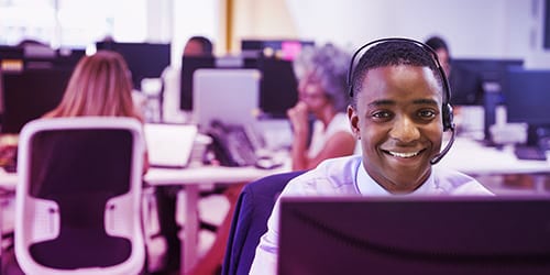 Young man working at computer with headset in busy office