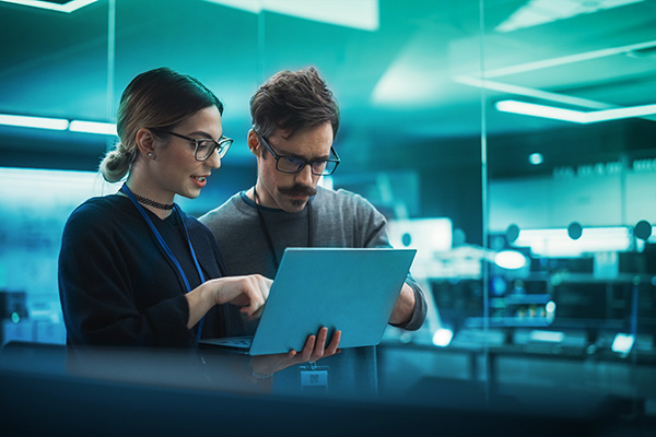 Portrait of Two Creative Young Female and Male Engineers Using Laptop Computer to Analyze and Discuss How to Proceed with the Artificial Intelligence Software. Standing in High Tech Research Office